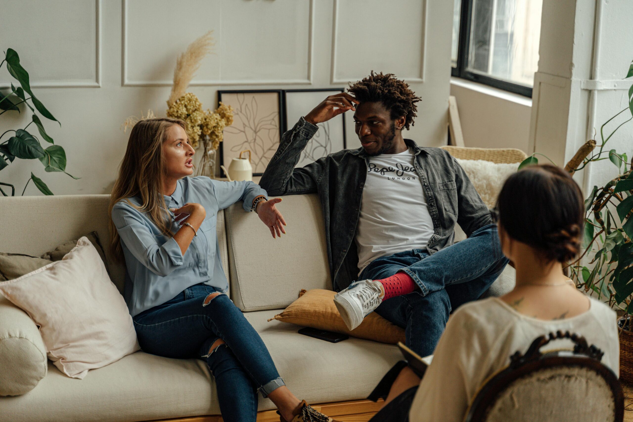 Image of couple looking at each other on couch with therapist sitting adjacent to them in therapist office.