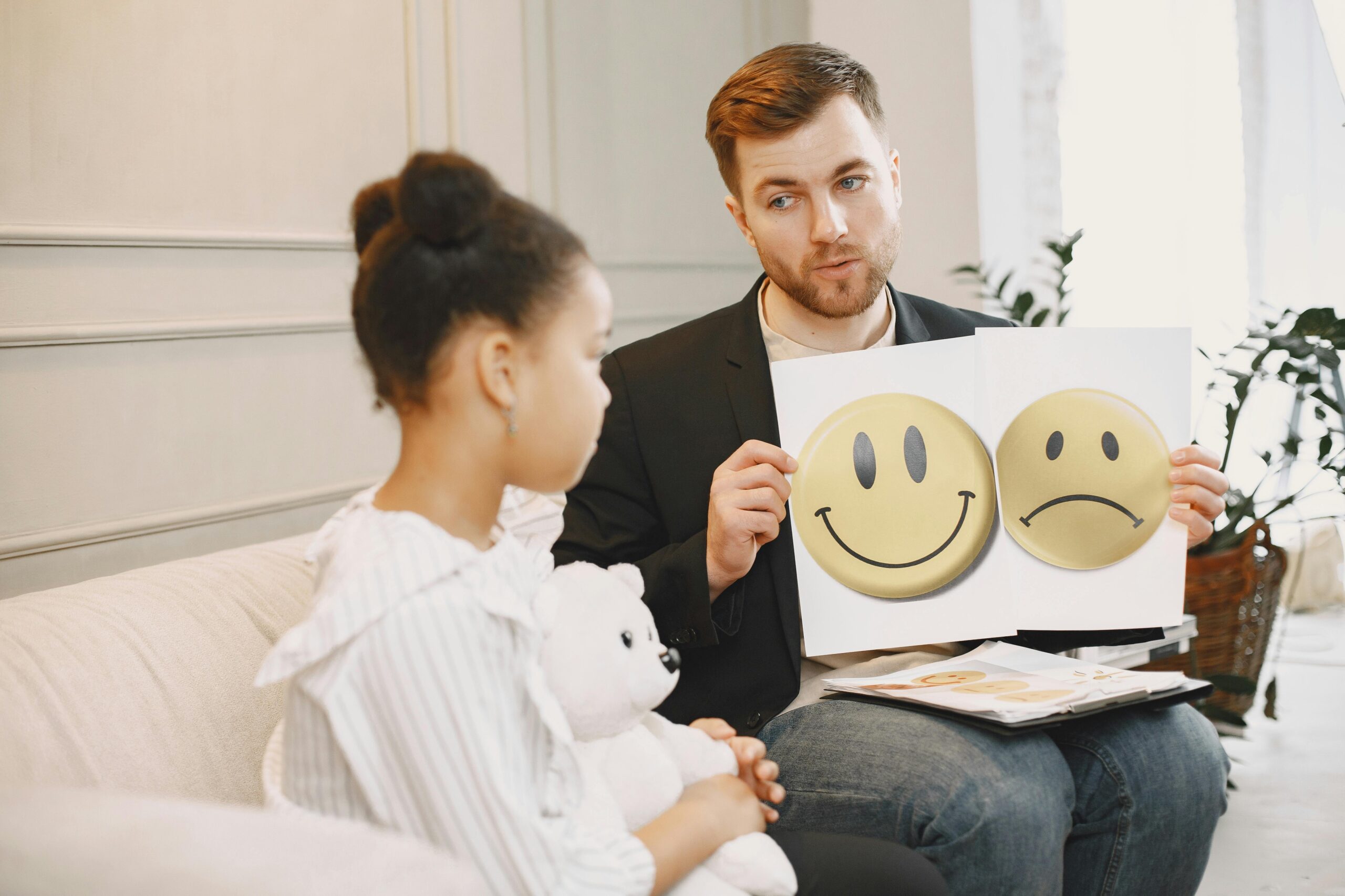 Image of therapist holding a happy face and sad face up to child in therapy session.