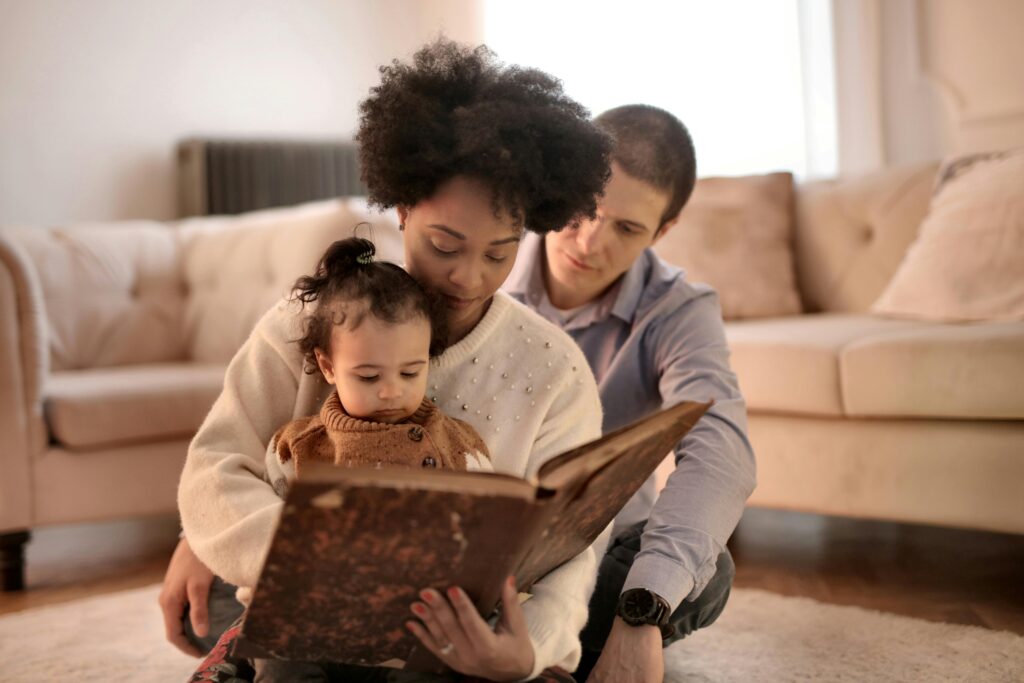 Image of parents holding child in their lap as they read the child a book.