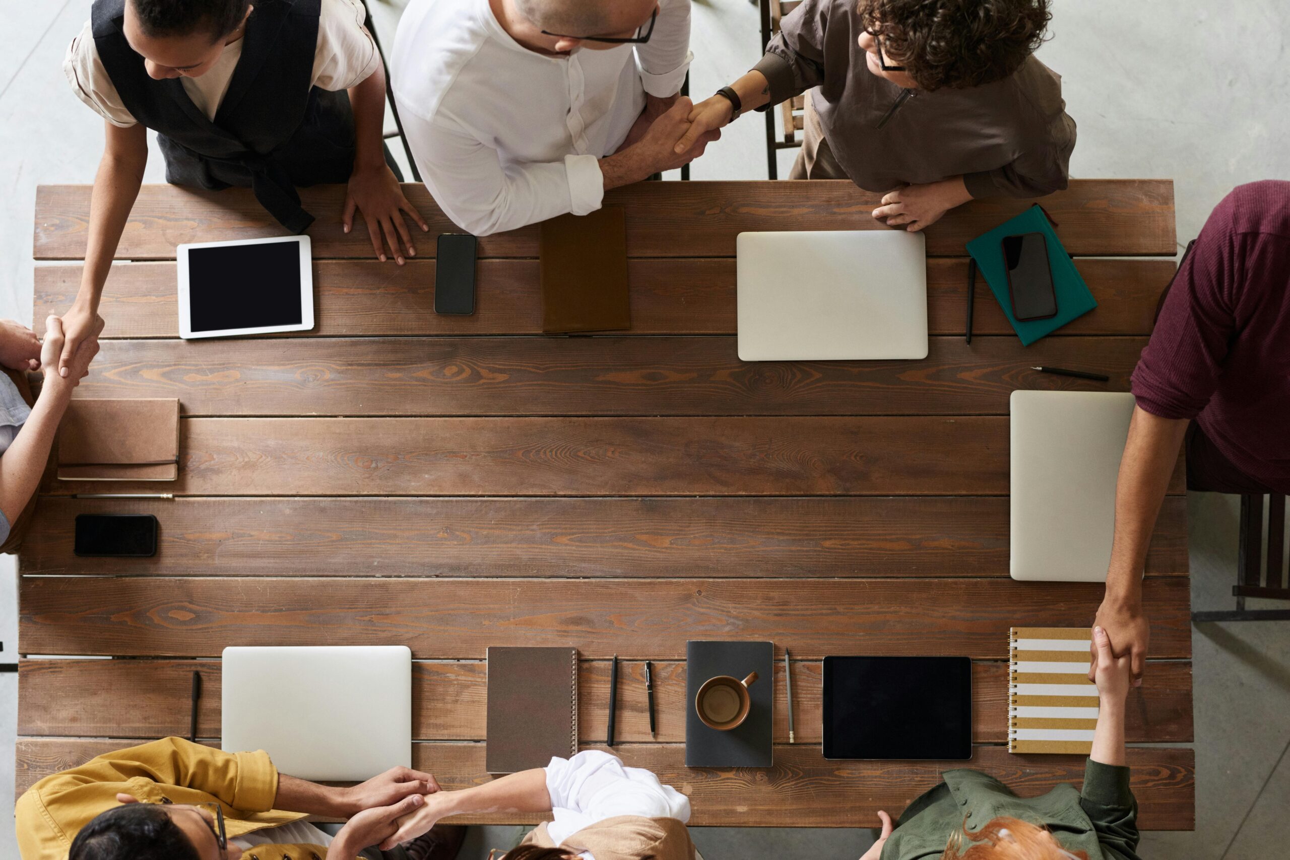 Image of eight people sitting around a table and all are shaking hands with one another, as a backdrop image to the words, "Group Therapy."