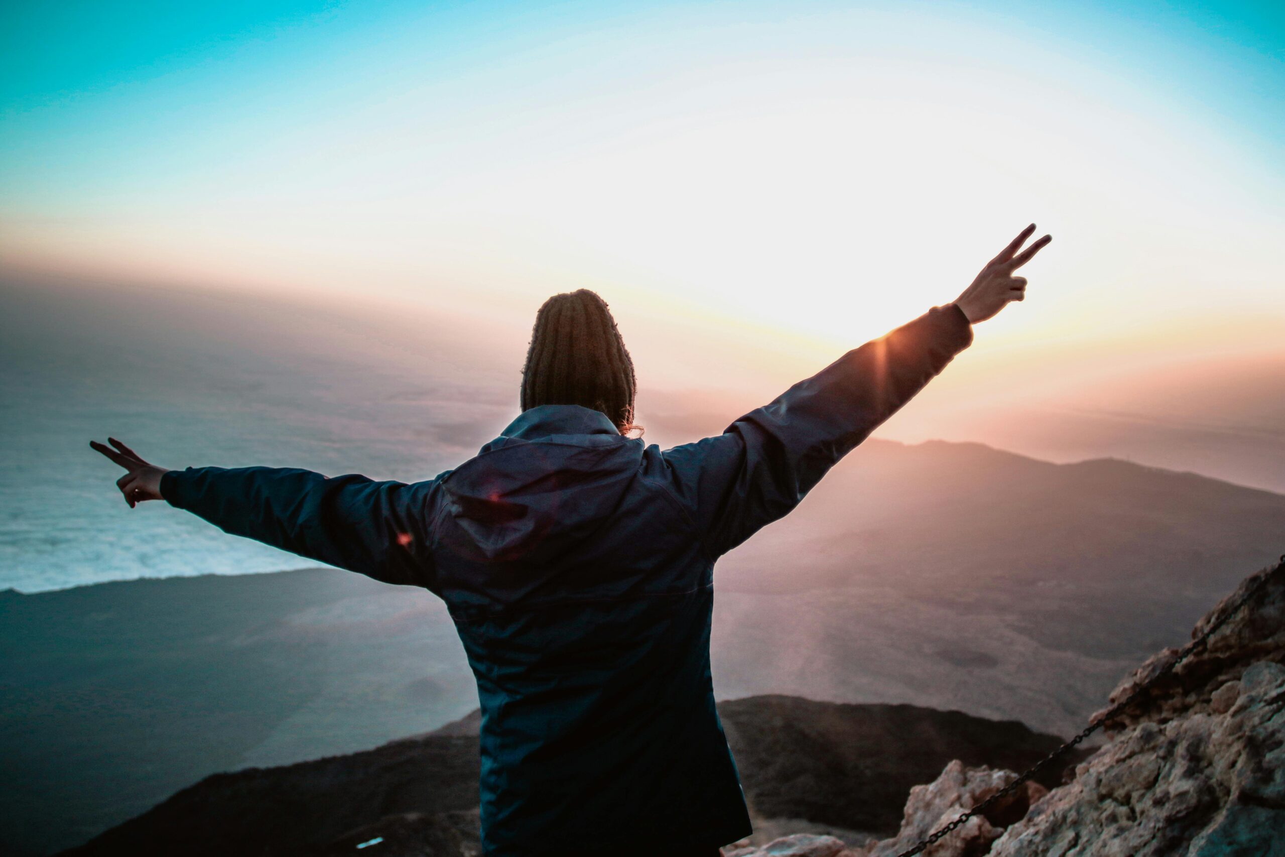 Image of person standing on mountain top with hands and arms spread out.
