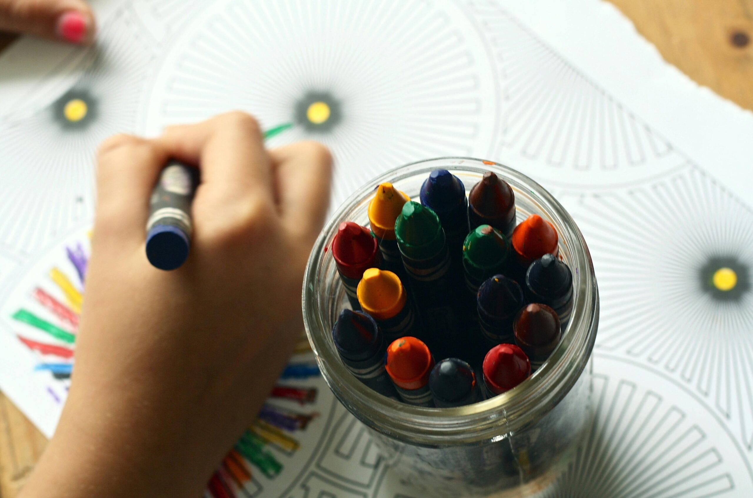 Image of child's hand using crayons to color picture and a glass cup with crayons in it, which serves as backdrop to the words, "Child & Adolescent Therapy."
