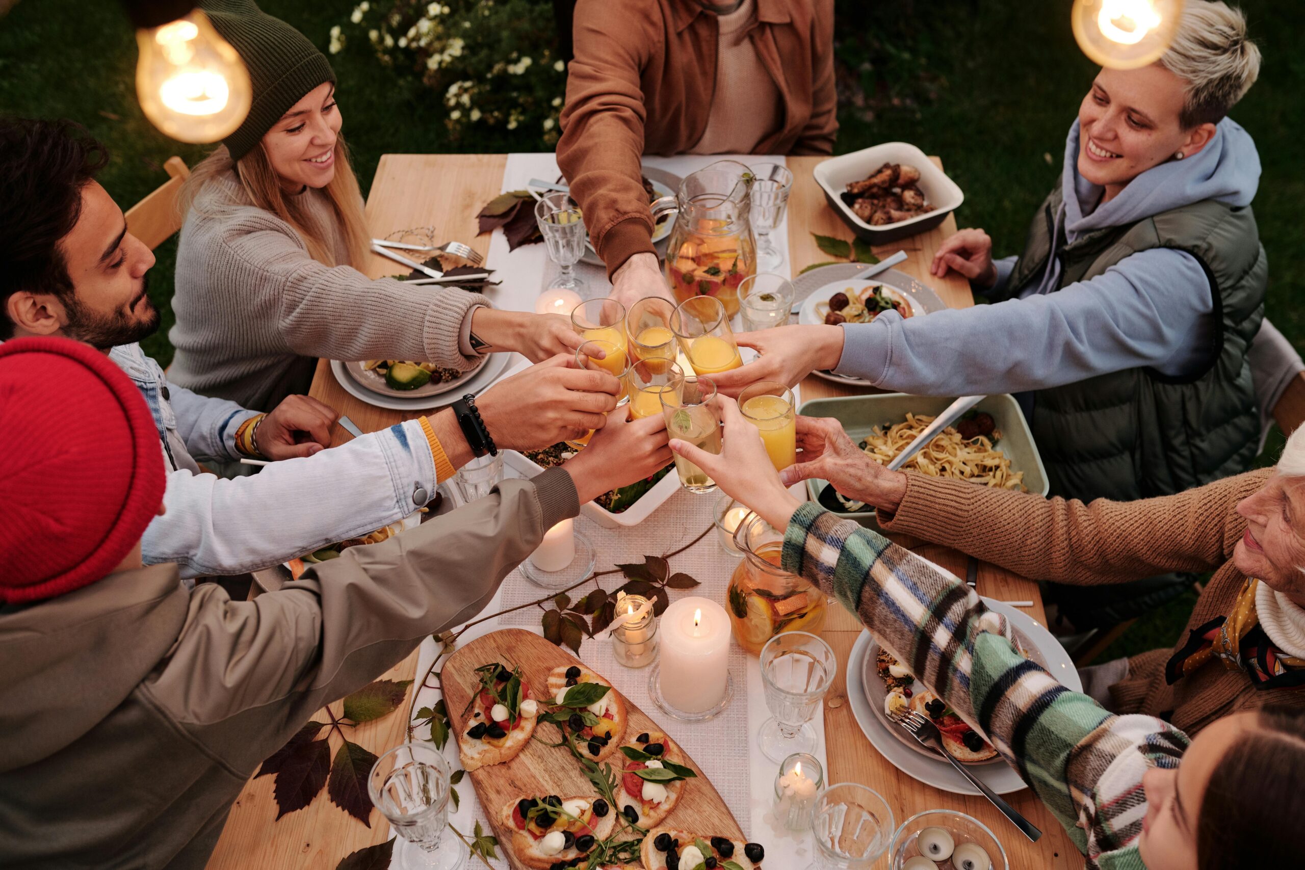 Image of family sitting around dinner table reaching together with glass in hand to engage in a "cheers" with one another.