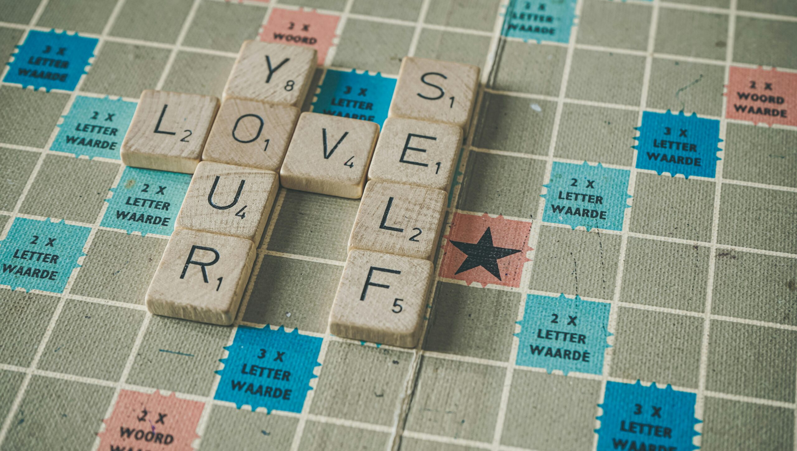 Image of Scrabble board and letters that connect, which read the three following words: "love your self."