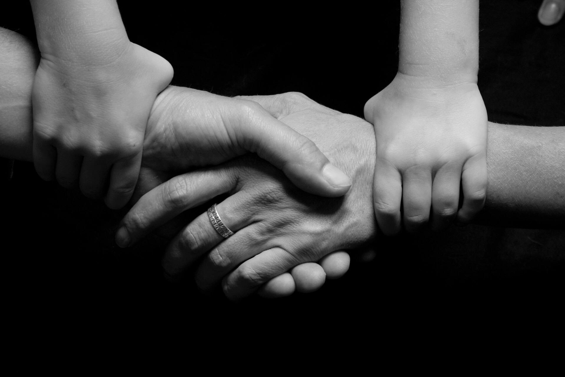 Image of child's hands holding parent's hands together.