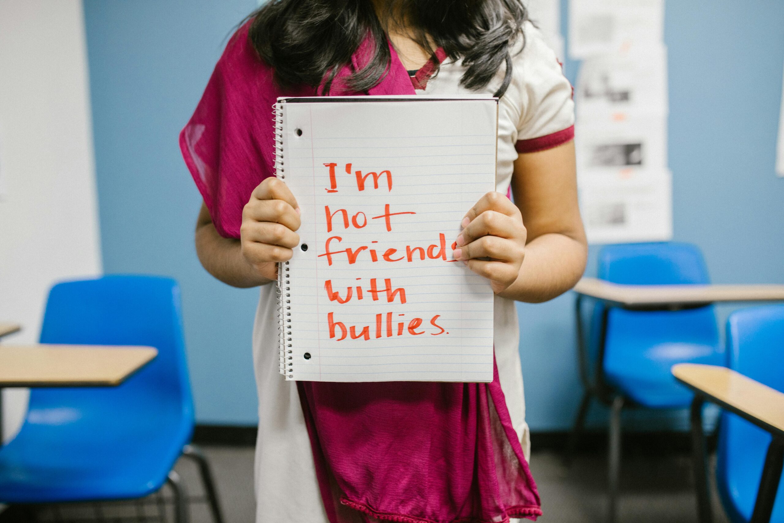 Image of girl holding up a notebook with the following words written on it: "I'm not friends with bullies."