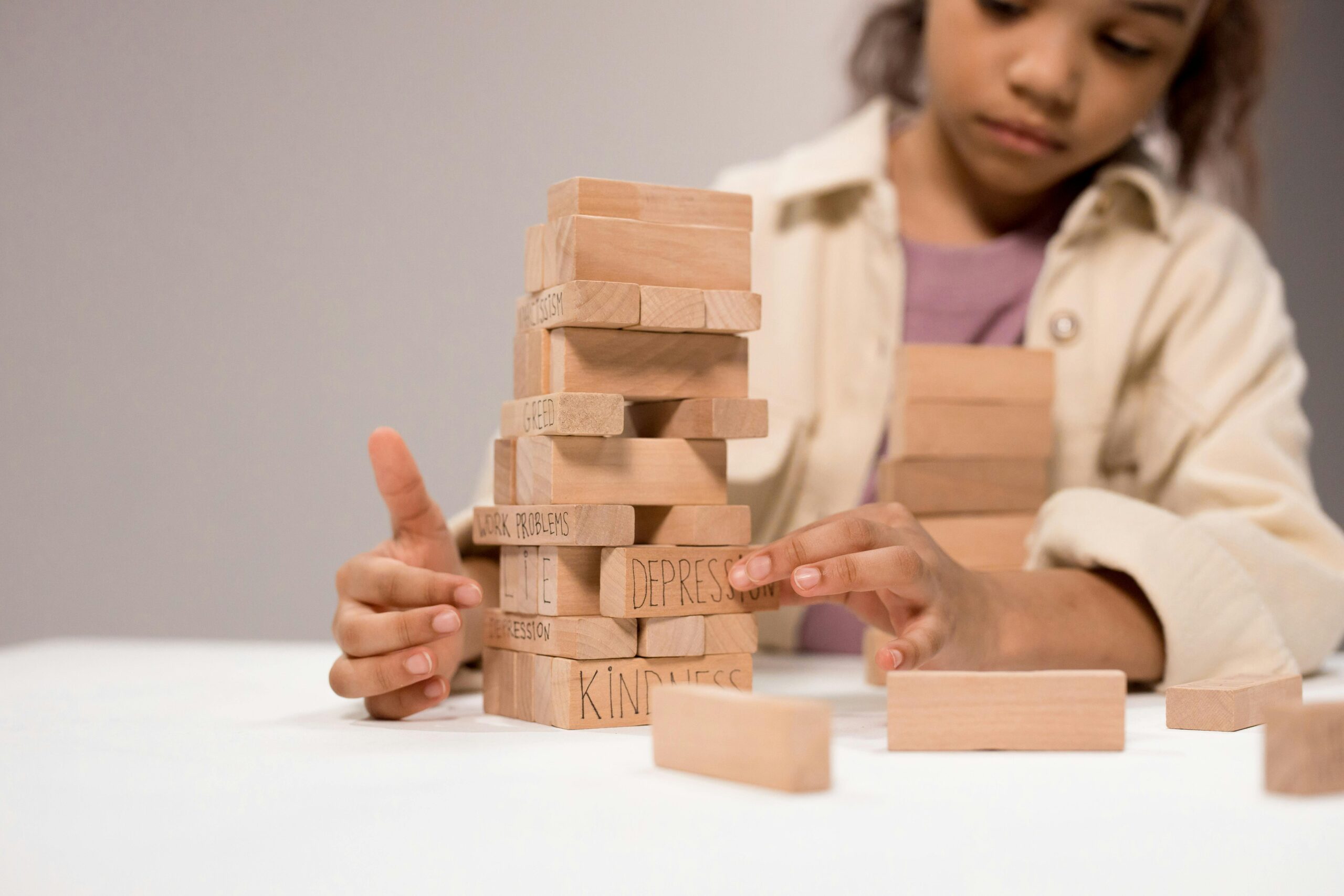 Image of child playing with Jenga wood block pieces that have the word "depression" written on one of the wood blocks.
